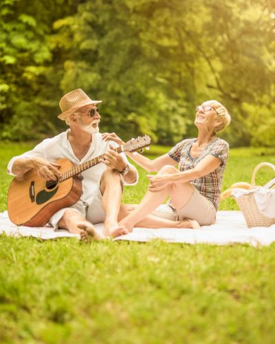 retired couple playing guitar and enjoying picnic